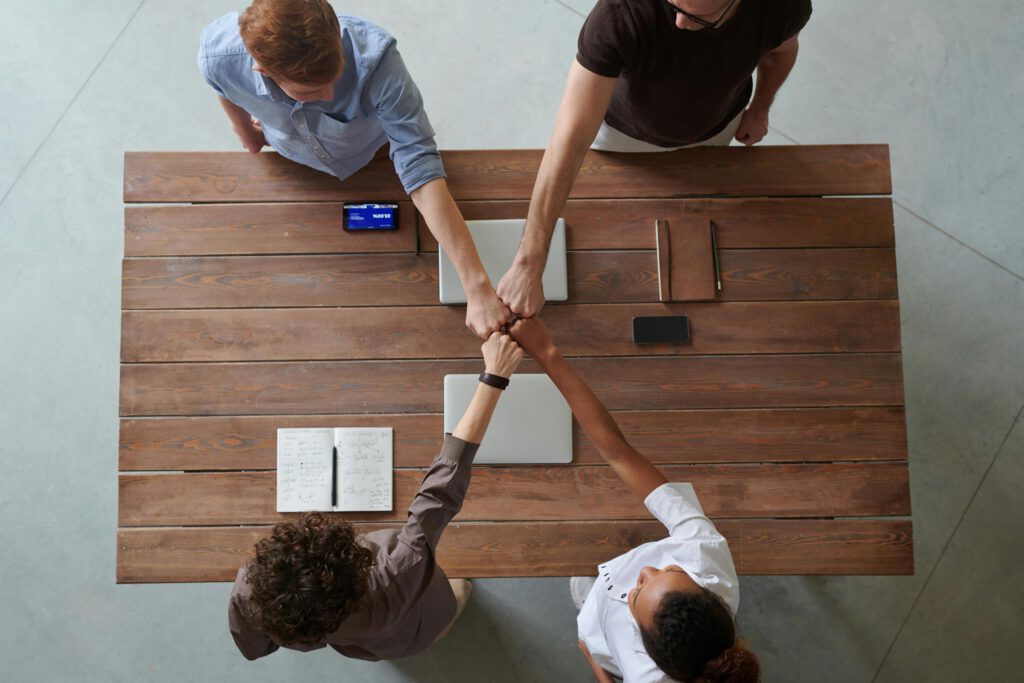 A diverse group of professionals engaging in a teamwork celebration with a fist bump over a wooden table indoors.